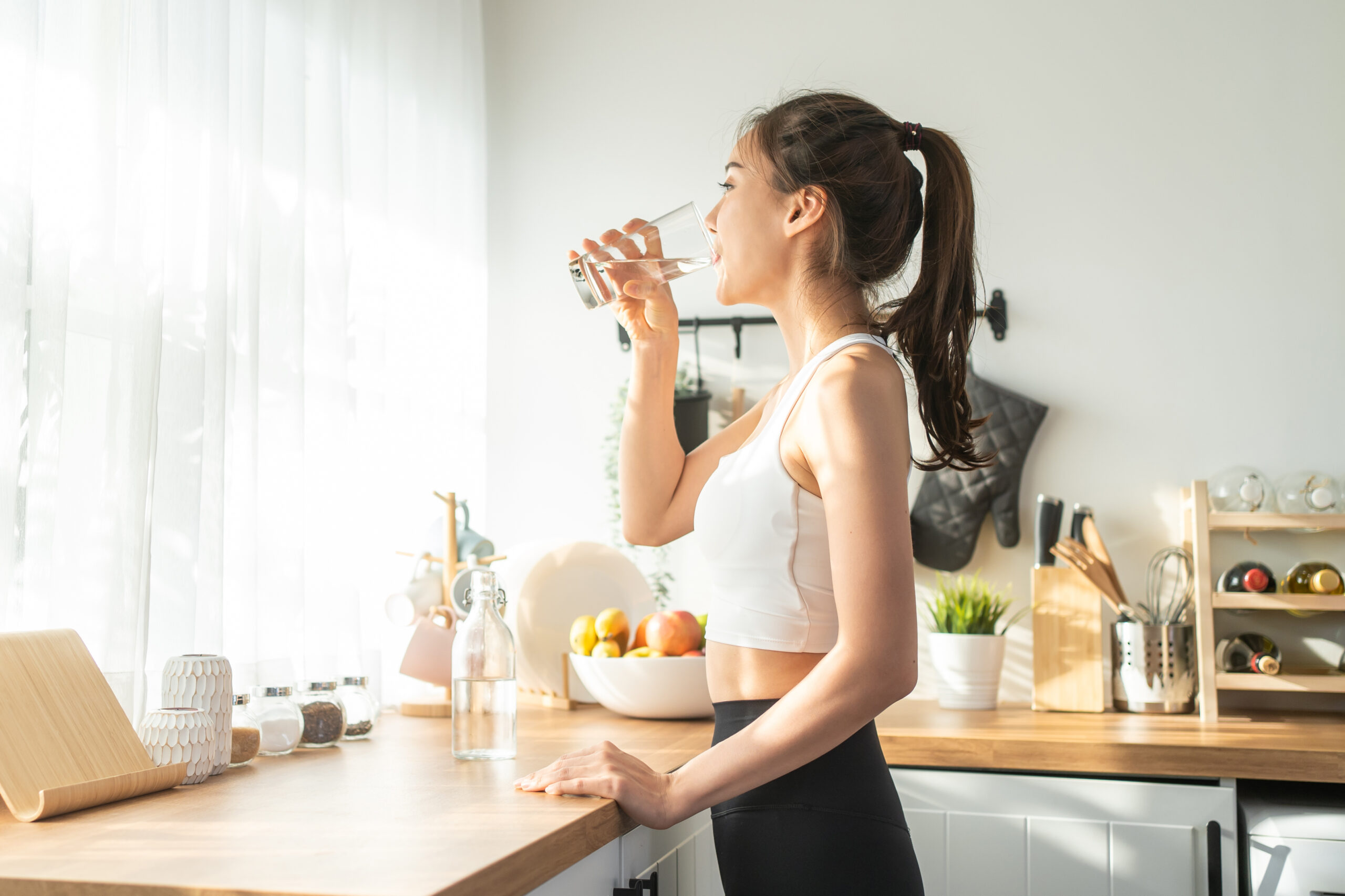 Asian beautiful woman in sportswear drink water after exercise a Asian beautiful woman in sportswear drink water after exercise at home. Young thirsty active sport girl takes a sips of clean mineral natural in cup after workout for health care in kitchen in house.