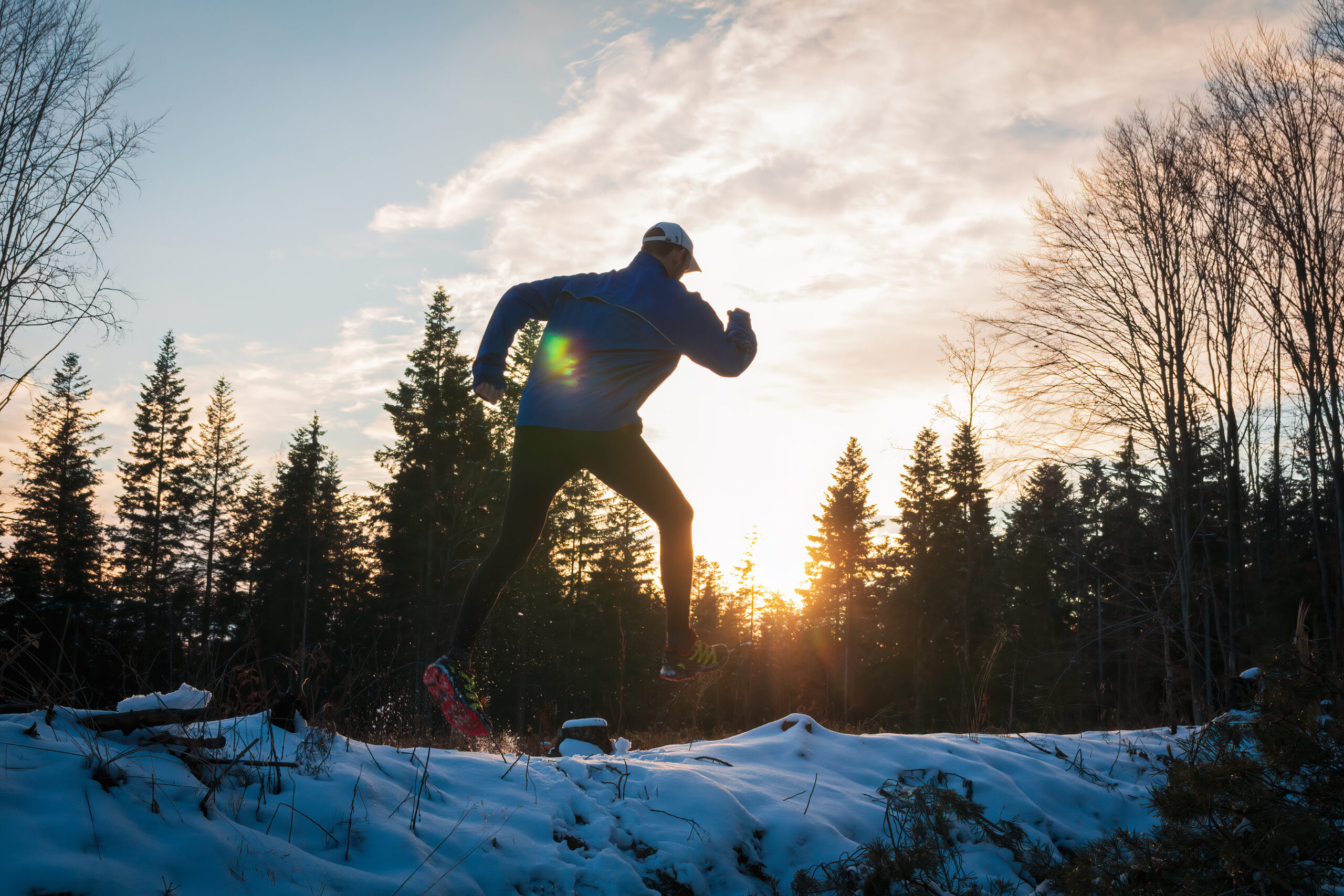 Young caucasian man running on snow in Czech winter landscape at sunset. Sport athlete in jacket, leggings and cap Young caucasian man running on snow in Czech winter landscape at sunset. Sport athlete in jacket, leggings and cap