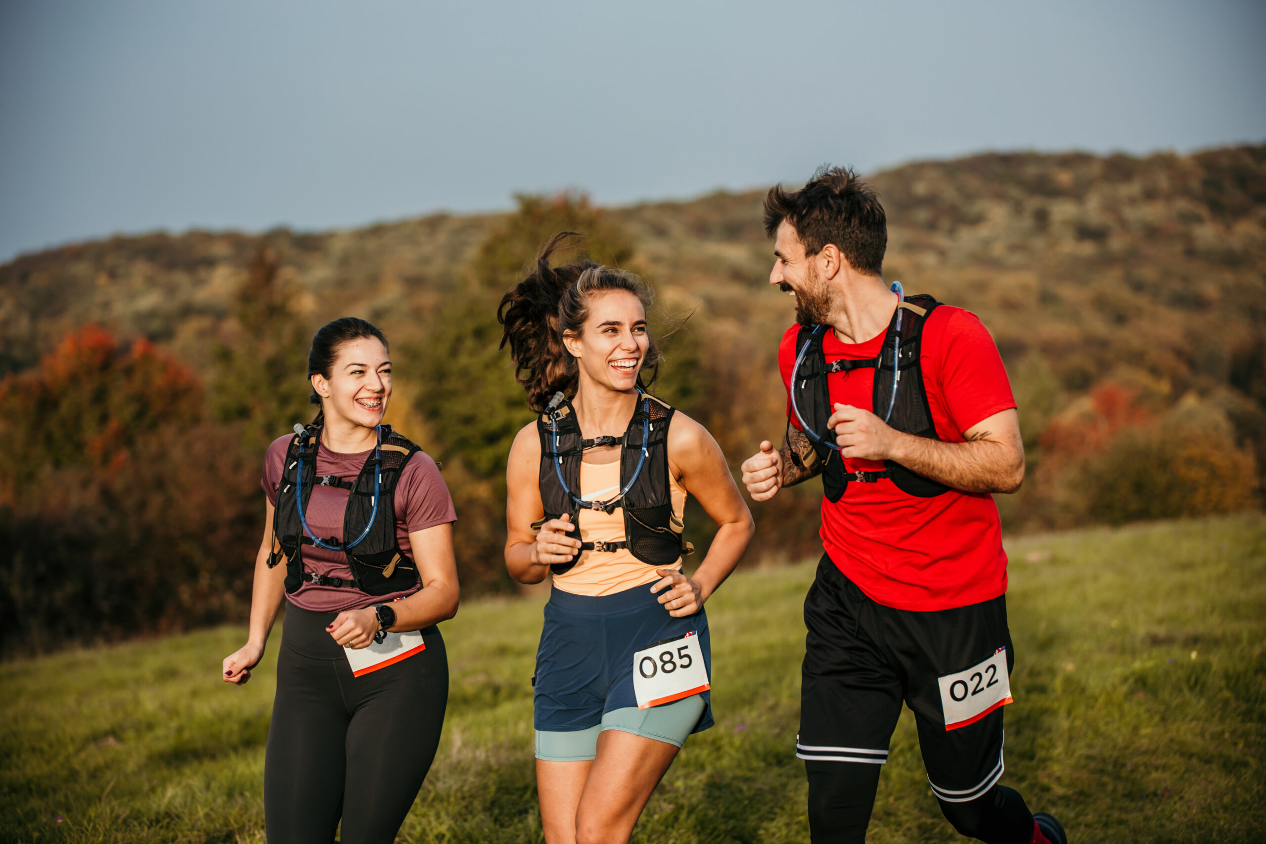 A small group of adults running in an outdoor cross-country race together. They are each dressed comfortably in athletic wear and have numbers pinned to the front of them as they focus A small group of adults running in an outdoor cross-country race together. They are each dressed comfortably in athletic wear and have numbers pinned to the front of them as they focus