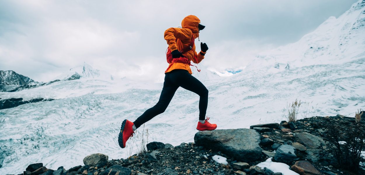 Woman trail runner cross country running up to winter snow mountain top